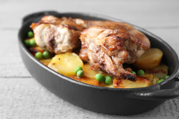 Tasty cooked rabbit with vegetables in baking dish on grey wooden table, closeup