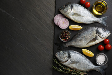 Fresh raw dorado fish, lemon, spices and tomatoes on black table, flat lay. Space for text