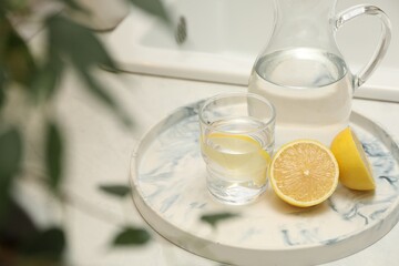 Jug, glass with clear water and lemons on white table in kitchen