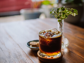Espresso tonic in a glass on cafe table. Coffee with tonic in a glass with ice on a light wooden background. Trendy summer craft refreshing drink. Front view.