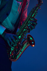 Jazz in modern music. Close-up cropped photo of young handsome man playing saxophone in neon light....