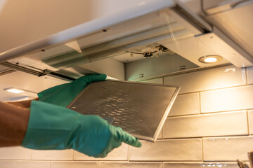 A person with rubber gloves removes an airfilter above a stove top for cleaning.