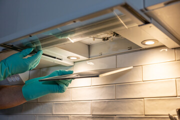 A person with rubber gloves removes an airfilter above a stove top for cleaning.