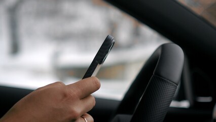  person sits behind the wheel of a car, holding a cell phone in their hand while driving. Unsafe driving.