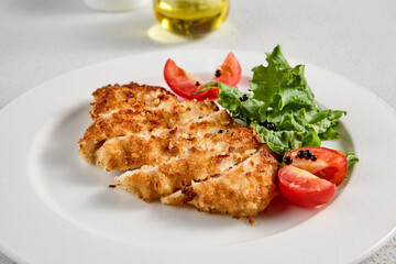 Golden crusted chicken fillet with cheese on a bed of lettuce, topped with cherry tomatoes, ideal for recipes and menu designs