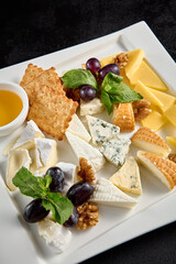 Cheese board with grapes and honey on a white plate against a black background