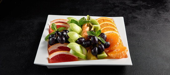 Seasonal fruit platter with grapes, orange, apple, and grapefruit on a white plate