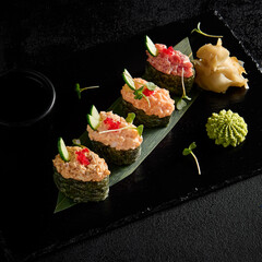 Spicy sushi assortment gunkan style with salmon, shrimp, tuna, and eel on a black slate