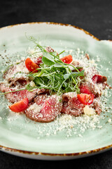 Roast beef carpaccio with Parmesan, arugula, and tomatoes on a speckled turquoise plate