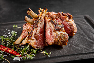 Perfectly grilled lamb rack served on a slate plate, with fresh herbs and a spicy red chili