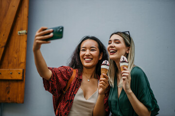 Chinese and Caucasian girlfriends savoring ice cream cones while taking photos in the heart of the city