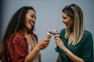 Two diverse female friends, one Chinese and one Caucasian, sharing laughter over ice cream in the...
