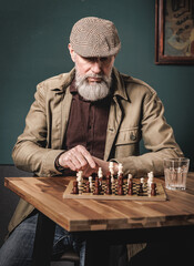 Portrait d'un homme agé avec une barbe jouant aux échecs en bois dans un bar en buvant un verre...