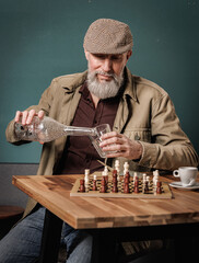 Portrait d'un homme avec un béret agé senior quinquagénaire qui boit de l'eau et un café et qui joue aux échecs sur une table en bois