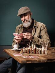 Portrait d'un homme quinquagénaire agé senior assi à une table qui joue aux cartes et aux échecs tout en buvant un café et un verre d'eau