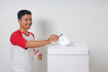 Portrait of excited Asian man inserting and putting the voting paper into the ballot box. General elections or Pemilu for the president and government of Indonesia. Isolated image on white background