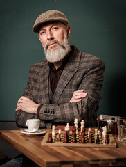 Portrait d'un homme quinqua hipster assis à une table avec un appareil photo argentique, un café et un jeux d'échec qui regarde droit devant lui