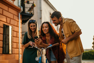 Diverse group of friends, Chinese and Caucasian, enjoying city exploration, leaning on a bike, and sharing a laugh while holding a smartphone