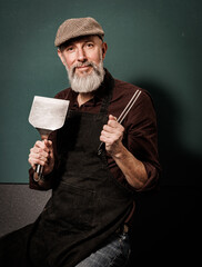 Portrait d'un homme barbu senior agé quinquagénaire hipster cuisinier qui tient des ustensiles de cuisine pour faire une plancha ou un barbenue