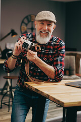 Portrait d'un homme debout photographe hipster situé dans un studio atelier et qui tient un appareil photo vintage en souriant devant un ordinateur