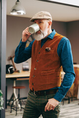 Portrait d'un homme chic hipster élégant et stylé et qui boit une tasse de café dans un atelier créatif
