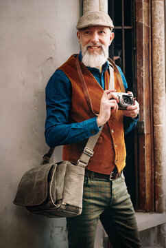 Portrait en extérieur dans une ruelle d'un homme photographe chic hipster élégant et stylé qui porte un appareril photo vintage argentique