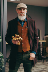 Portrait d'un homme original gentleman quinquagénaire senior hispter élégant et stylé avec un manteau un béret et un gilet dans un atelier créatif