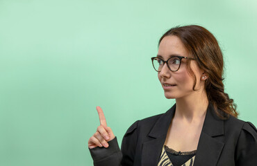 A woman in eyewear and a black business jacket points at a peppermint color empty background. Copy space for text. 