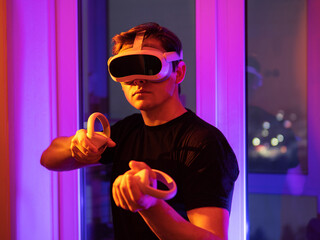 A young man in a virtual reality headset and gamepads with controllers, playing a shooting game. Modern technology, play VR video games.