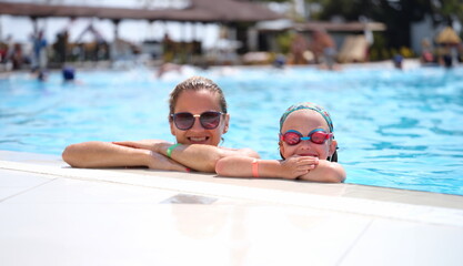 Little girl in swimming goggles and mother lying on side of pool. Rest with children in water park concept