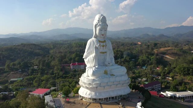 Aerial circling around Wat Huay Pla Kang giant white big statue and pagoda temple with mountains and landspace in Chiang Rai, Thailand.
