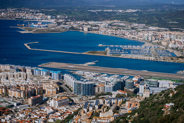 Fototapeta na wymiar Gibraltar, Britain - January 24, 2024 - An aerial view of a densely built coastal city with a marina, an airport runway near the sea, industrial areas, and mountains in the background.