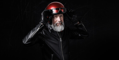 Portrait d'un motard homme avec un casque et une veste en cuir et des lunettes de protection et une barbe grise vintage