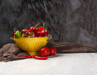 Mock up photo on a white wooden table with a yellow enameled colander with fresh red, green peppers, chilies and tomatoes
