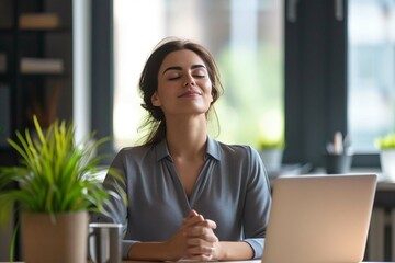 Happy employee getting ready to start productive work day. Young business woman sitting at office desk and meditating eyes closed thinking of good things and focusing on positive feelings and emotion