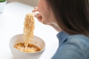 Fotobehang Young female eating instant noodle isolated on background. © Pormezz