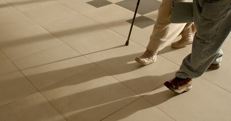 Mobility and independence of seniors. Elderly couple strolling with support of cane in sunny indoors. No face. Issues associated with aging. Aged couple walking together.