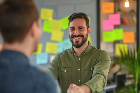 Casual Business Collaboration. Smiling man in green shirt discussing with a colleague in a creative workspace with sticky notes.