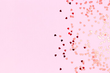 Metallic red confetti in a heart shape scattered on a pink background. Composition with copy space.