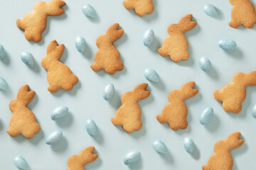 Easter glazed cookies shaped of bunny and chocolate blue eggs on blue background. View from above. Festive food and snacks. Easter pattern.