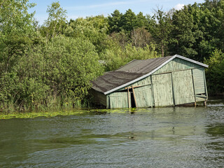 Ein marodes hölzernes Bootshaus versinkt in einem Gewässer - 724630575