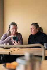 Senior women looking at cell phones together in a pastry shop