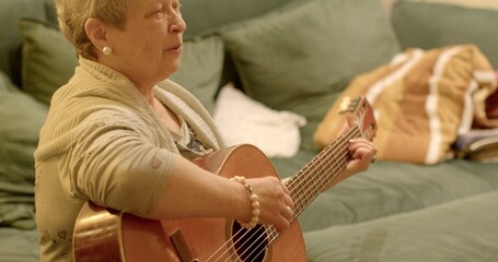Portrait of happy mature woman playing cheerful tunes on guitar. Playing the guitar involves...