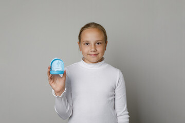 Happy young child girl holding invisalign transparent retainers with a blue box on white studio wall  background