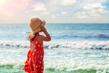 Happy little girl walking on the beach in summer. A girl in a pink dress with polka dots and a...