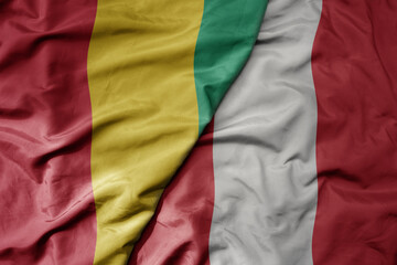 big waving national colorful flag of peru and national flag of guinea .