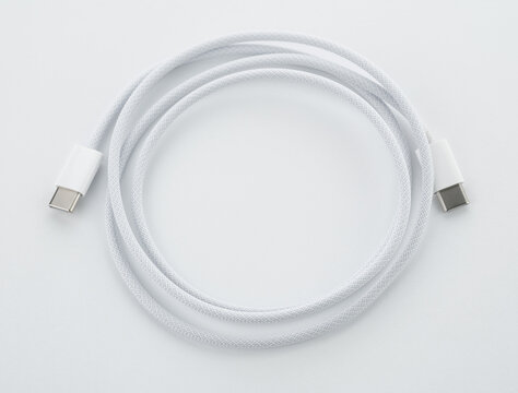 A white USB type C charger cable, compatible for many devices, wrapped in a spiral shape, isolated on white background. White simple USB lightning cable, rolled up