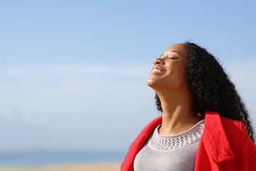 Happy black woman breathing fresh air on the beach in winter