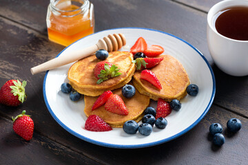 Pancakes with fresh berries and honey on a wooden table