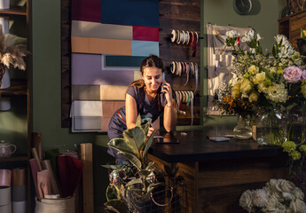 Young woman working in her flower shop talking on the phone and receiving an order for a bouquet of flowers.